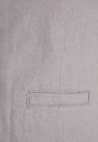 Un tissu gris avec une texture diagonal présente une poche rectangulaire cousue. La poche a des bords nets et des coutures assorties.