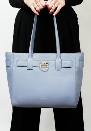 Sac fourre-tout en cuir bleu clair avec anses doubles, présentant un accent en métal doré de forme circulaire et une texture lisse.