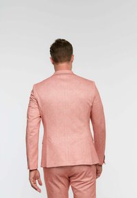 Svijetloružičasta jakna od odijela s teksturiranim materijalom, slim fit dizajnom i reverima. Sadrži minimalno šivanje i odgovarajuće hlače.