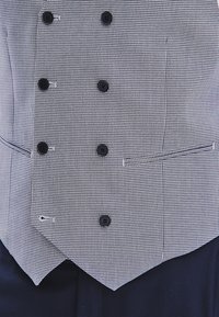 Czarnobiały kamizelka w wzór houndstooth z sześcioma guzikami, wyciętymi klapami i detalem kieszeni. Tkanina ma gładką teksturę.