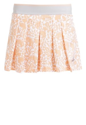 Vrouw draagt een wit mouwloos topje, perzikkleurige bloemen geplooide rok en witte sneakers met roze zolen, staand op één been.