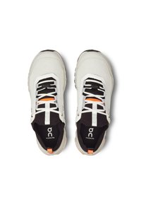 Baskets blanches avec un dessus en maille texturée, un intérieur noir, des lacets noirs, des accents oranges et une semelle épaisse. Logo notable sur la languette.