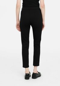 Pantaloni neri su misura con una vestibilità aderente, pieghe frontali e una texture liscia, abbinati a mocassini neri in pelle. Design minimalista.