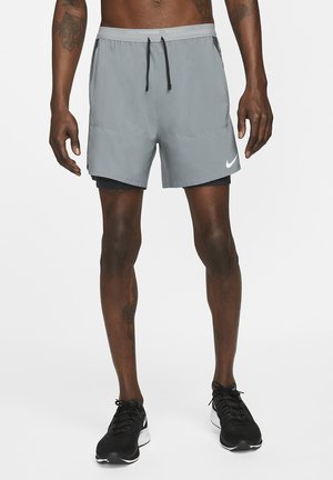 Pantalones cortos deportivos grises con cintura ajustable, bolsillos laterales y forro interior negro, combinados con zapatillas de correr negras con detalles blancos.