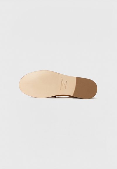 Suela de zapato de cuero beige con una superficie lisa y bordes redondeados. Presenta una sutil marca y una sección de tacón contrastante en marrón.