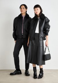 Μαύρες δερμάτινες bomber τζάκετ με γιακά από γούνες, φορεμένα πάνω από μαύρη μπλούζα και φούστα. Συνδυασμένα με μαύρα τζιν και παπούτσια. Απλός, κομψός σχεδιασμός.