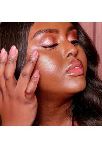 Applicazione del trucco su un incarnato caldo. Le caratteristiche includono labbra glossate, ombretto glitterato e unghie lunghe e naturali con smalto rosa chiaro.