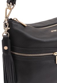 Zwarte leren handtas met een gestructureerde afwerking, goudkleurige hardware, een ritscompartiment en een kwastaccent.