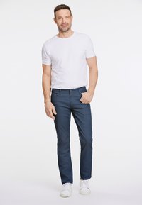 Weißes T-Shirt mit kurzen Ärmeln, kombiniert mit navyblauen Slim-Fit-Hosen mit einem dezenten Muster und frontalen Taschen, abgerundet mit weißen Sneakers.