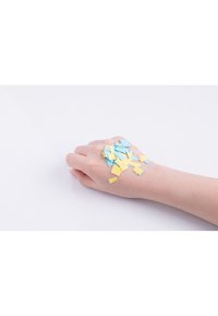 Hand med ljus hy som visar spridda blå och gula geometriska papperskonfetti på en enfärgad vit bakgrund.