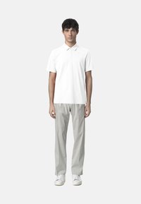 Polo shirt bianco con maniche corte e colletto, abbinato a pantaloni grigi chiari. Completato da sneaker bianche, in piedi su uno sfondo neutro.