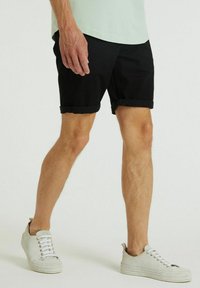 Pantaloni corti neri con risvolti realizzati in tessuto leggero, dal taglio classico. Indossati con scarpe da ginnastica chiare e una maglietta verde menta.