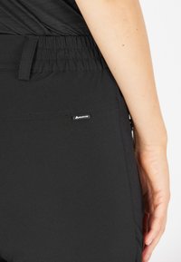 Svarta träningsbyxor med en rynkad midja, sidoficka och en liten logotagg. Slät tyg med matt yta.