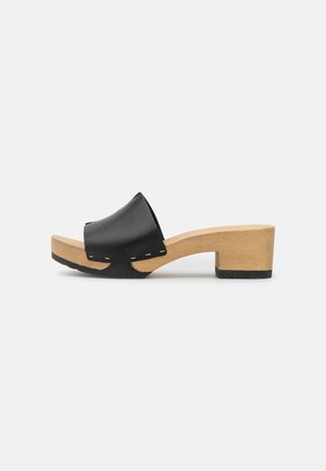 Mule femme à bout ouvert avec dessus en cuir noir et petit talon bloc en bois sur fond blanc.