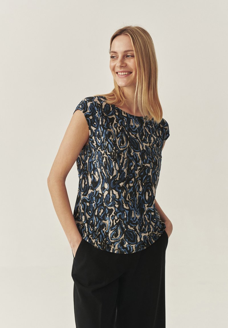 Top a maniche corte con motivo astratto blu e nero, in tessuto morbido, scollo rotondo e vestibilità comoda, abbinato a pantaloni neri.