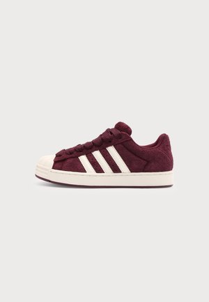 Bordowy zamszowy sneaker z białym gumowym noskiem, białą podeszwą i trzema białymi paskami po boku, widziany z prawej strony.
