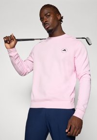 Sweatshirt rose à manches longues et col rond, avec un petit logo sur la poitrine. Tissu lisse au fit décontracté.
