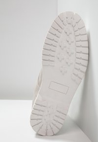 Suola di sneaker bianca in gomma testurizzata, con un motivo di forme incrociate; design pulito, bordi leggermente curvi e taglia 42 contrassegnata.