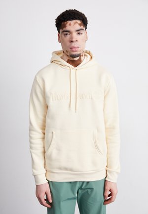 Cream hooded sweatshirt with embroidered "Timberland" logo. Features a front pocket and ribbed cuffs, paired with green pants.