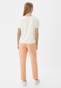 Weißes kurzärmliges Hemd, kombiniert mit sanften Pfirsich-farbenen, taillierten Hosen und weißen Sneakers. Glatte Texturen und ein einfaches Design ohne Verzierungen.