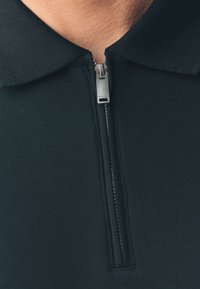 Zwart poloshirt met ritsen met metalen trekker, een getextureerde kraag en een effen, gladde stof.