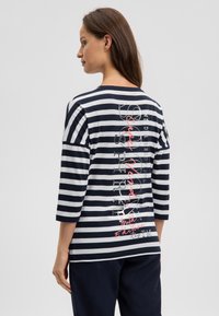 Striped t-shirt with three-quarter sleeves, navy and white colors, featuring graphic text in red and black on the back. Soft cotton material.