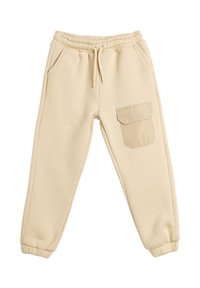 Pantalones de chándal beige hechos de material suave, con cintura elástica, bolsillos laterales y un bolsillo de parche en la pierna derecha.