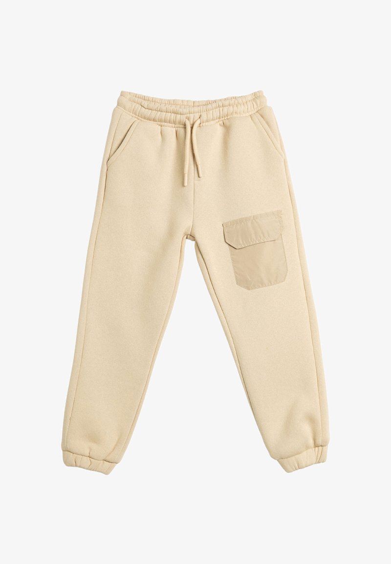 Pantalones de chándal beige hechos de material suave, con cintura elástica, bolsillos laterales y un bolsillo de parche en la pierna derecha.