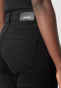 Zwarte spijkerbroek van denim met een fitted ontwerp, achterzakken en een leren label met het merk "MOS MOSH." Soepele textuur.