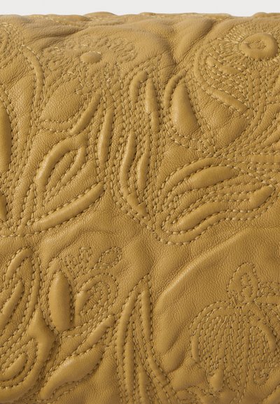 Couro amarelo com padrões em relevo de flores e folhas; apresenta costura intrincada e uma superfície suave e texturizada.