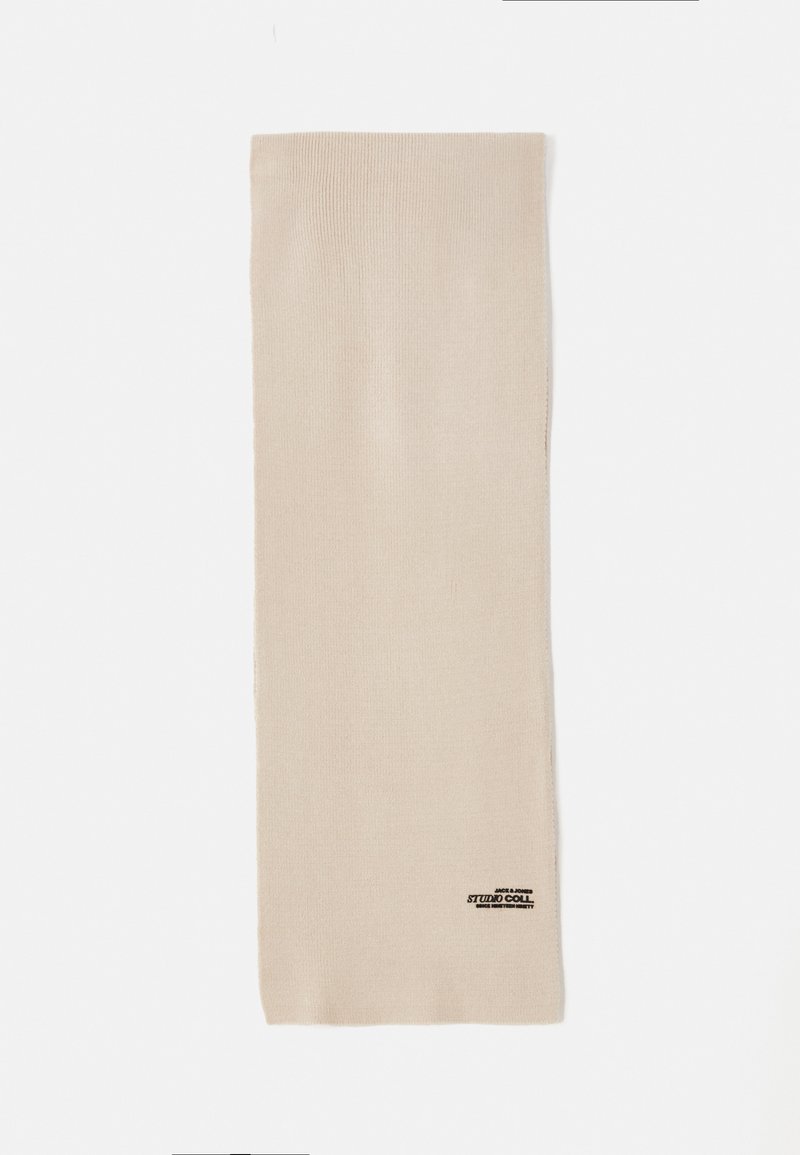 Beige gebreide sjaal met een zachte textuur, rechthoekige vorm, voorzien van een klein zwart logo label in de rechterbenedenhoek.