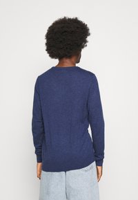 Navy long-sleeve shirt made of textured fabric. Features a rounded neckline and slim fit, with a slightly curved hem at the back.