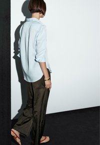 Lichtblauw, losvallend shirt met opgerolde mouwen, gecombineerd met donkere, wijde broek; eenvoudige sieraden en sandalen. Minimalistische stijl.