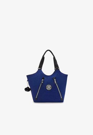 Blue fabric tote bag with black straps, featuring a round logo, two side zippers, and a black pom-pom accessory attached.