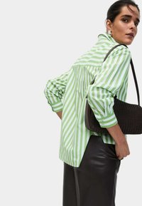 Gestreept shirt in groen en wit, met lange mouwen en een relaxed fit; gecombineerd met een bruine gevlochten handtas en een zwarte leren rok.