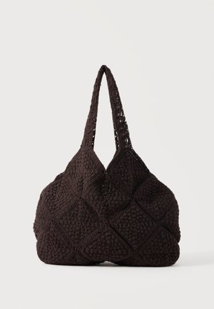 Sac cabas noir au crochet avec motifs carrés texturés et deux bretelles, posé sur un fond uni.