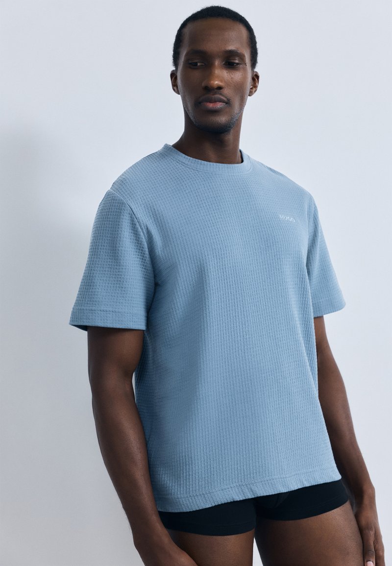 Világoskék rövid ujjú, texturált póló kerek nyakkivágással. Egyszerű dizájn, kis logó a mellkason és laza szabás.