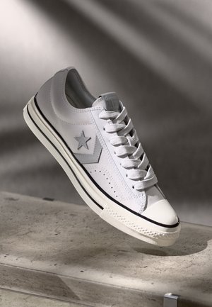 Baskets blanches avec une tige en cuir lisse, logo en forme d'étoile et bout arrondi. Présente des accents gris, une semelle texturée et des lacets plats.