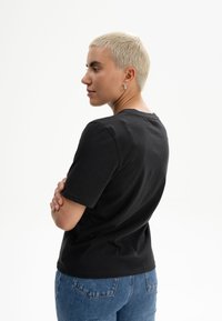 Schwarzes Baumwoll-T-Shirt mit Rundhalsausschnitt und kurzen Ärmeln, kombiniert mit blauen Jeans. Einfaches und klassisches Design, ohne sichtbare Muster.