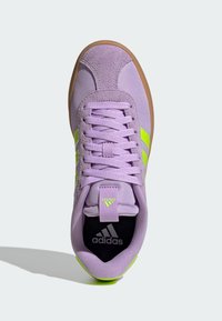 Jasnofioletowy sneaker z cholewką ze skóry zamszowej i tkaniny, neonowozielonymi paskami po bokach oraz gumową, brązową podeszwą. Model z wiązaniem na sznurowadła i wyściełanym kołnierzem.