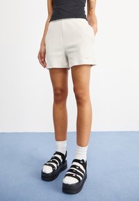 Vita ribbade shorts med hög midja, kombinerade med svarta och vita platåsandaler med iögonfallande logoband och vita strumpor.