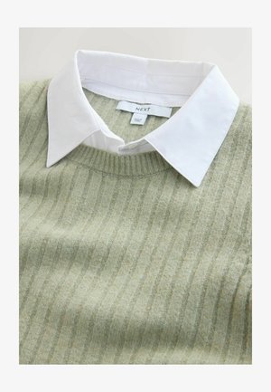 Svetlozelený sveter s vertikálnym rebrovaním, okrúhlym výstrihom a pod ním biela košeľa s golierom. Štítok s pokynmi na starostlivosť viditeľný pri krku.