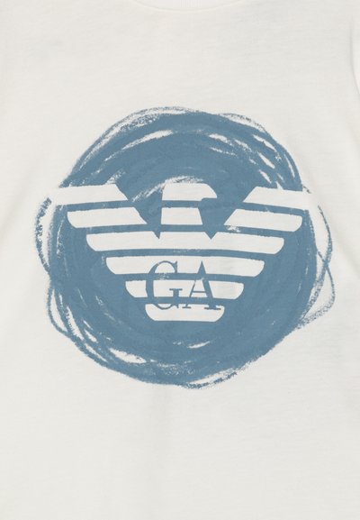 T-shirt bianca in cotone con un design grafico blu di un'aquila con strisce e le lettere "GA" in un motivo circolare a pennellate.