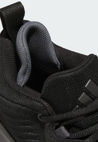 Interior de zapatilla deportiva negra con malla texturizada, lengüeta acolchada y forro gris. Incluye cordones negros y detalle de marca en el costado.