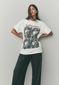 Hvid bomulds t-shirt med fire monokrome billeder med grafisk tryk af musikere, parret med sorte bredbenede bukser.