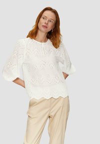 Witte geborduurde blouse met uitgesneden bloemenpatronen en een gebogen zoom. Kenmerkt zich door 3/4 pofmouwen en een knoopsluiting aan de nek.