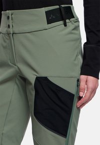 Lichtgroene outdoorpantalon met een zwarte mesh pocket, platte tailleband en zijrits. Glad textuur en aansluitend ontwerp voor mobiliteit.