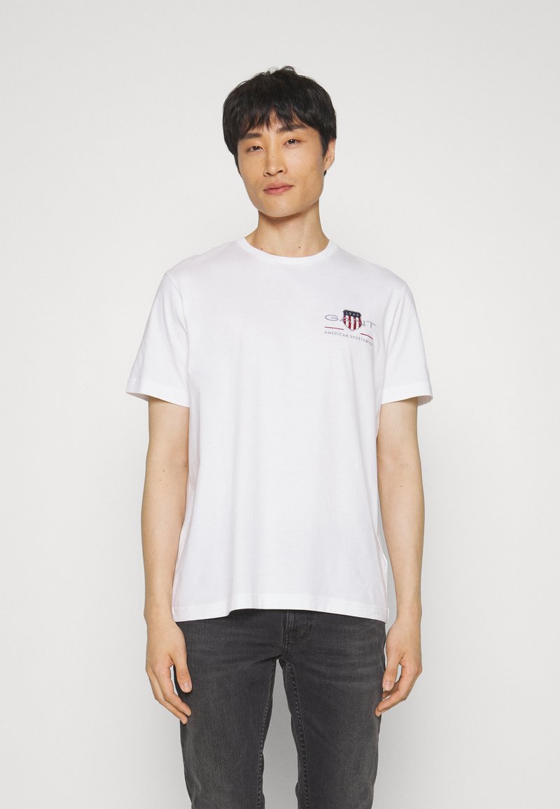 T-shirt en coton blanc à manches courtes, col rond et logo sur la poitrine gauche en rouge et bleu. Assorti avec un jean sombre. Design simple.