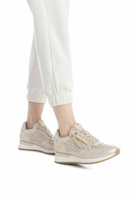 Zapatillas deportivas beige con diseño perforado, acentos dorados y suela blanca. Cuentan con un zipper lateral y punta redondeada para mayor comodidad y estilo.