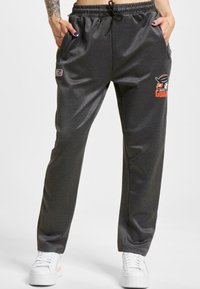 Mørkegrå sweats med glat stof og afslappet pasform. Har sidelommer og et grafisk logo i orange og sort på låret.
